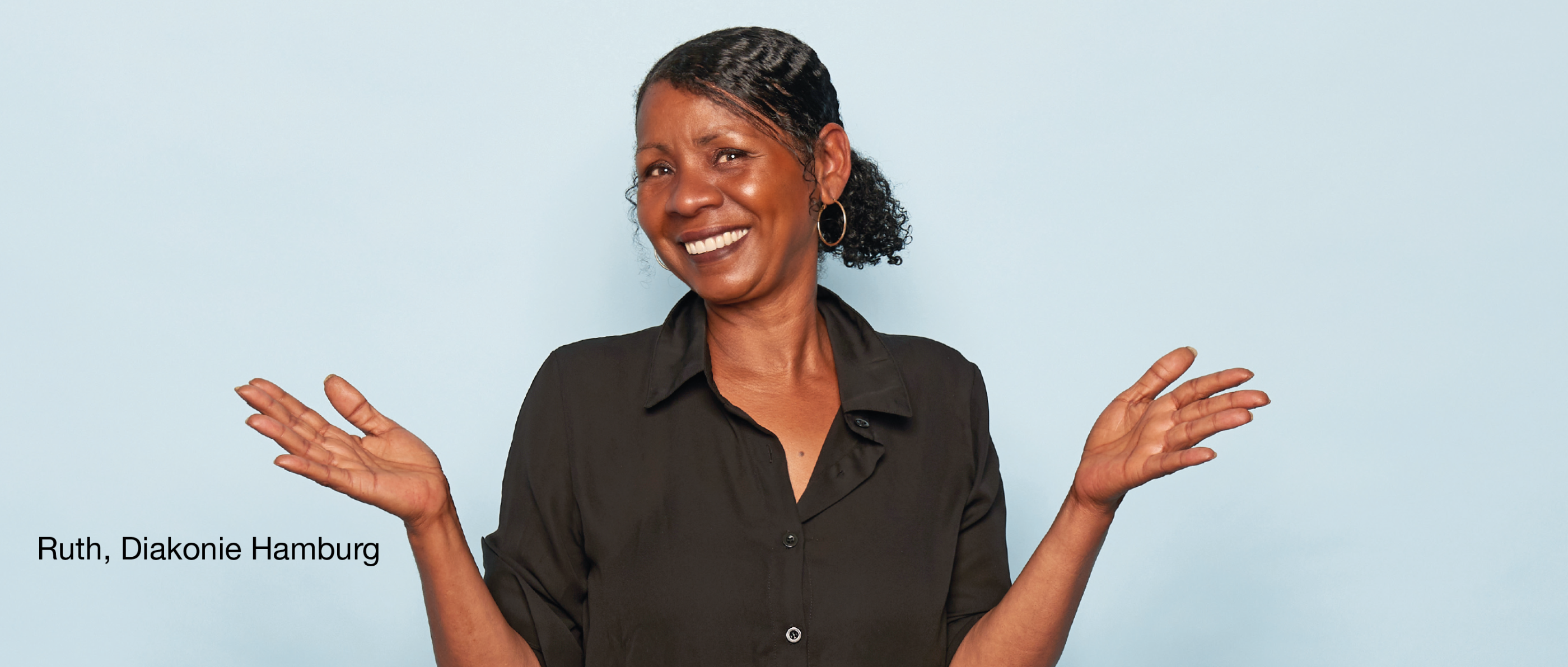 Person im schwarzen Hemd hebt beide Hände leicht vor hellblauem Hintergrund. Unten rechts steht „Ruth, Diakonie Hamburg“.