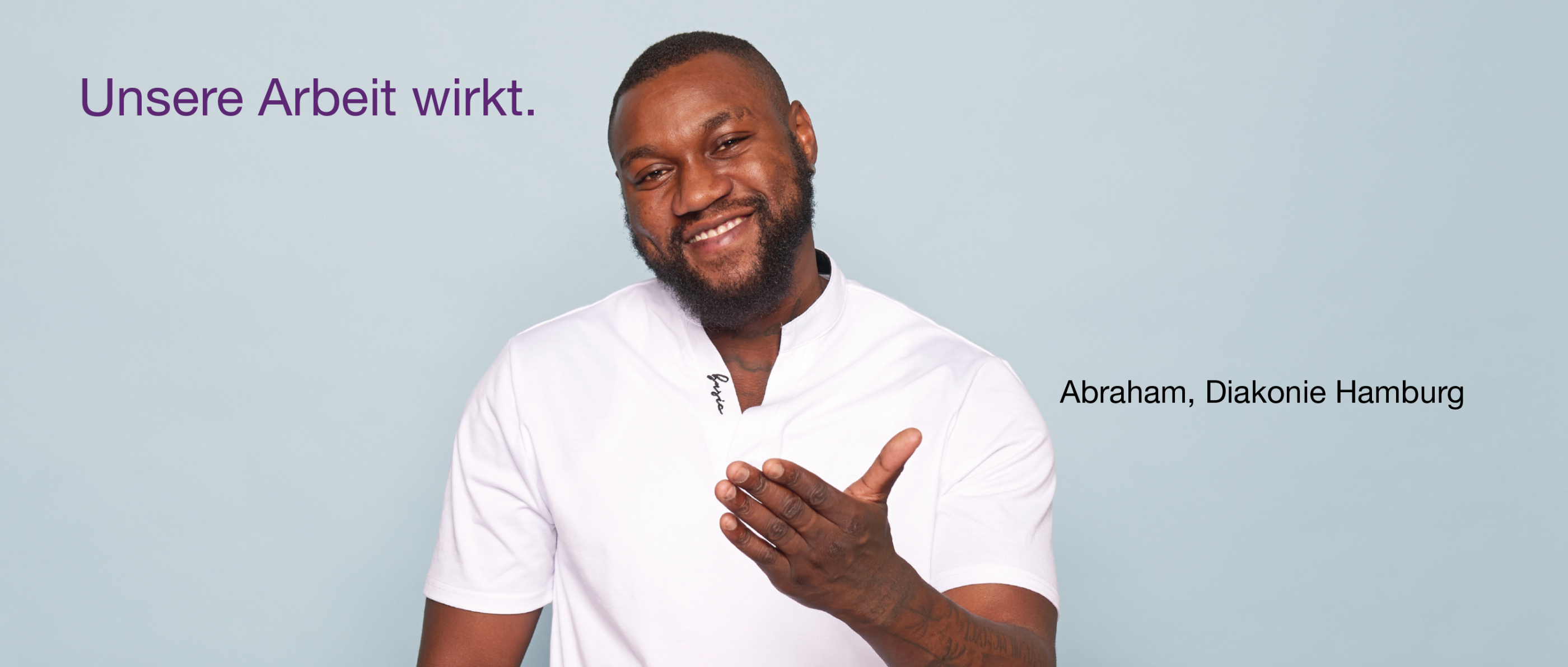 Person im weißen Hemd hebt eine Hand leicht vor hellblauem Hintergrund. Oben links in lila Schrift: „Unsere Arbeit wirkt.“, unten rechts: „Abraham, Diakonie Hamburg“.