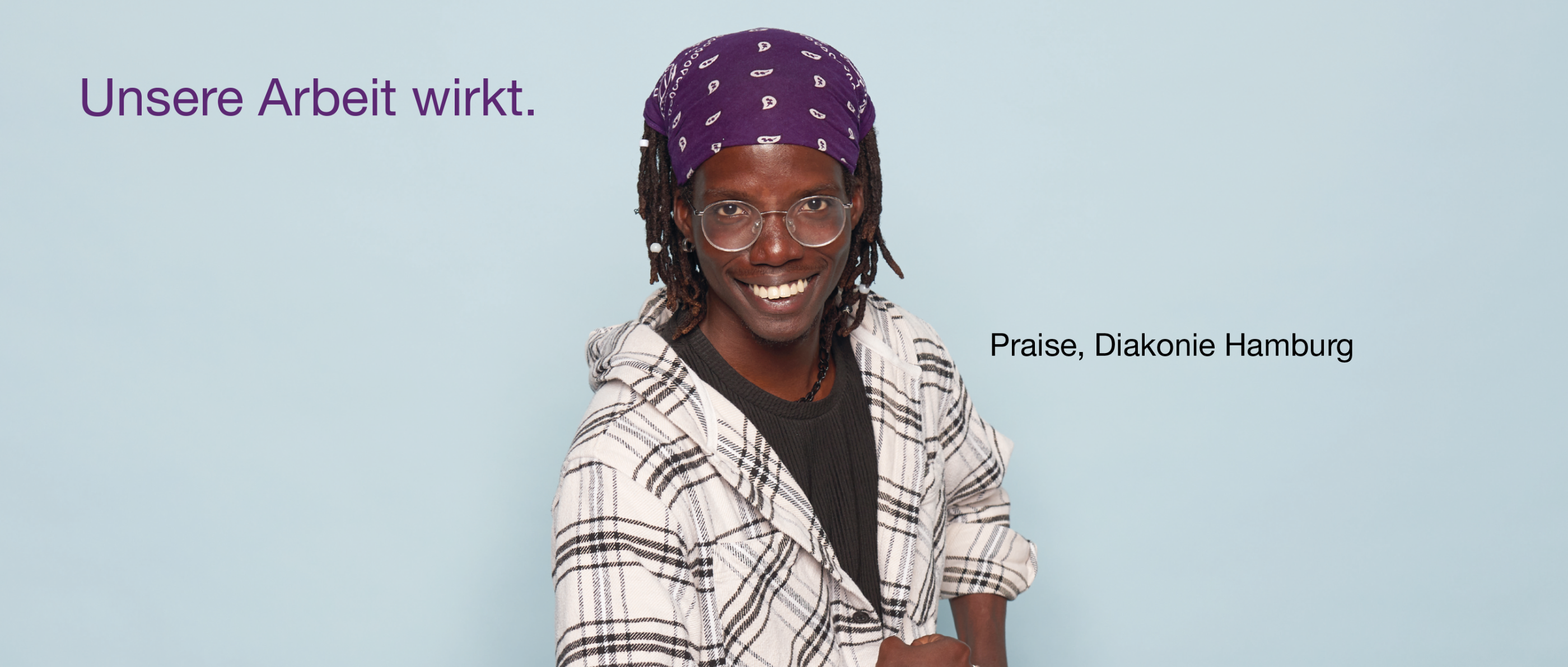 Person mit lila Bandana und karierter Jacke vor hellblauem Hintergrund. Oben links in lila Schrift: „Unsere Arbeit wirkt.“, unten links: „Praise, Diakonie Hamburg“.
