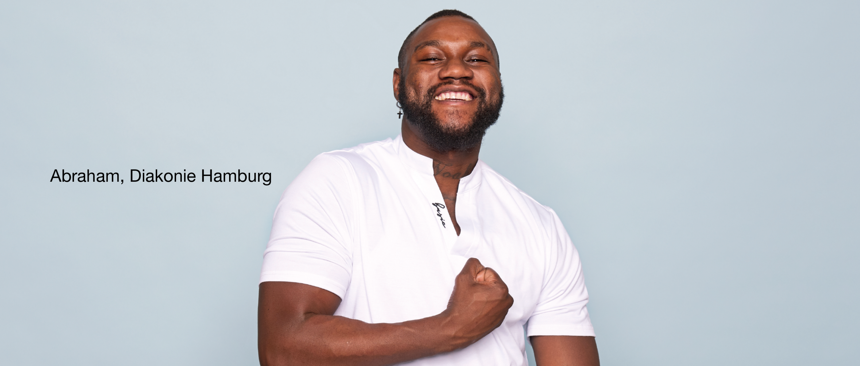 Person im weißen Hemd vor hellblauem Hintergrund hält eine Hand vor der Brust. Links Text 'Abraham, Diakonie Hamburg'.