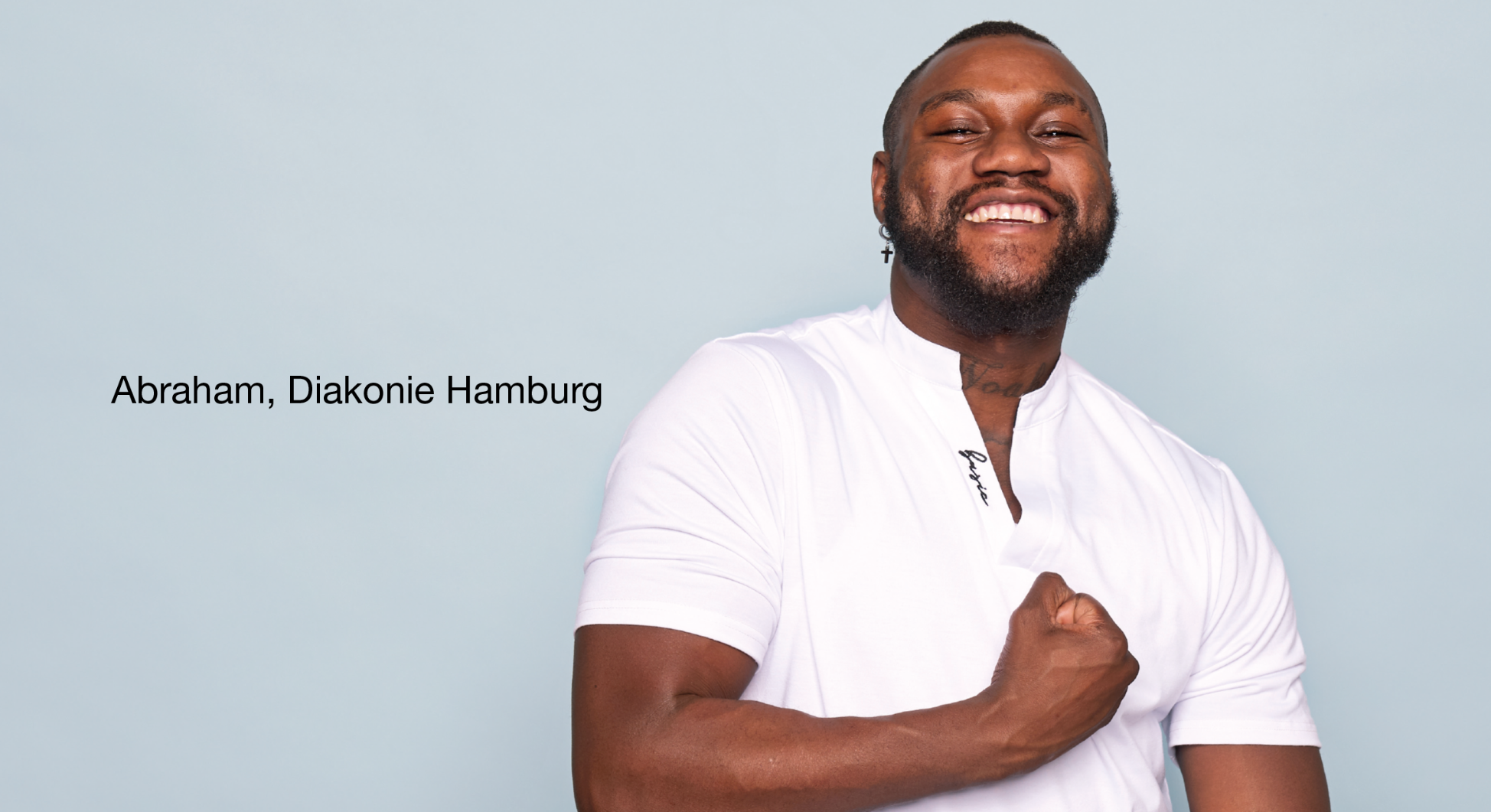 Person im weißen Hemd vor hellblauem Hintergrund hält eine Hand vor der Brust. Links Text 'Abraham, Diakonie Hamburg'.