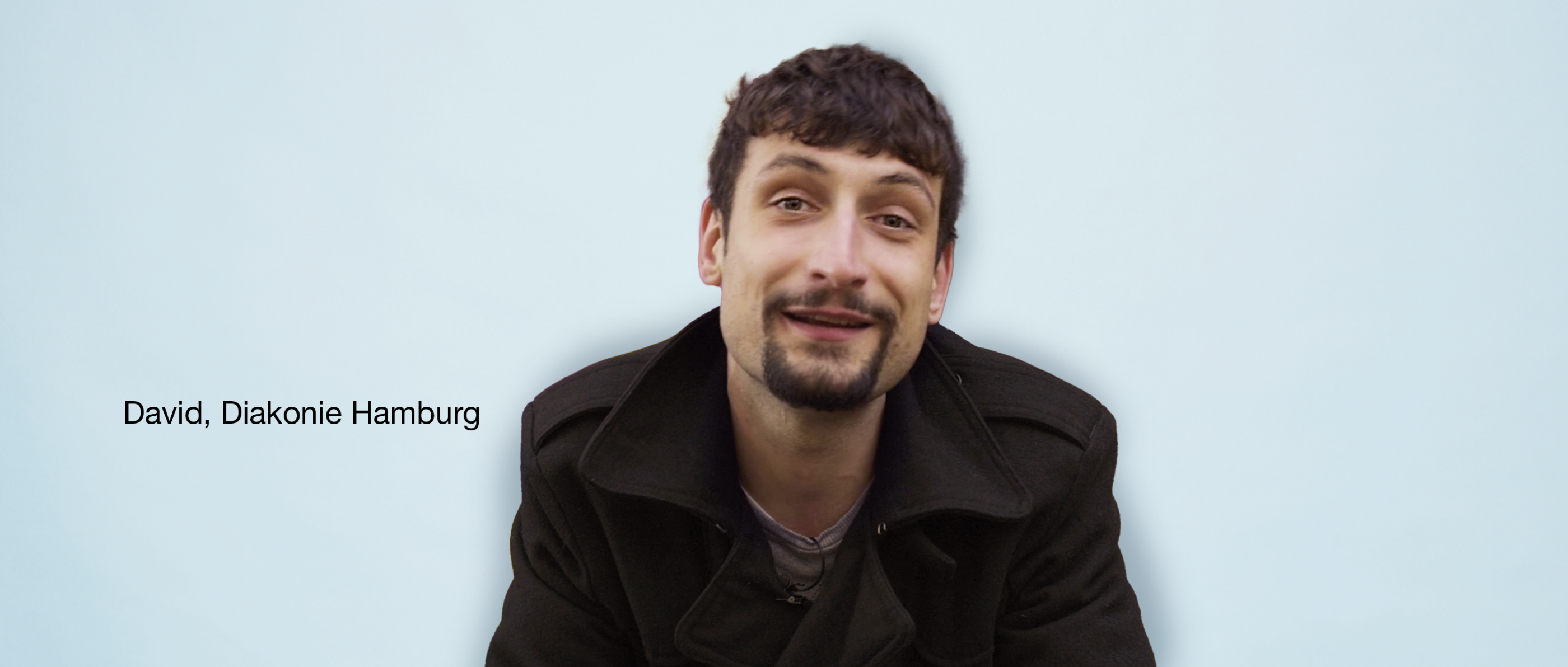 Person mit Bart und schwarzer Jacke vor hellblauem Hintergrund. Text links: 'David, Diakonie Hamburg'.