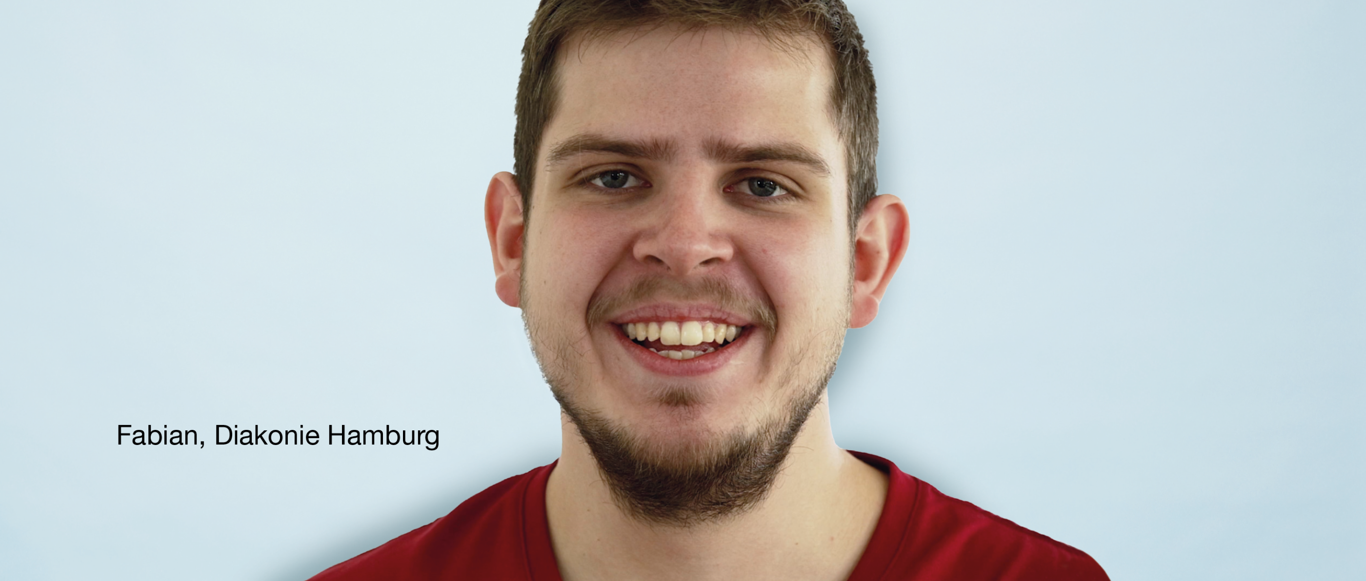 Person mit kurzem Haar und Bart im roten Shirt vor hellblauem Hintergrund. Text links: „Fabian, Diakonie Hamburg“.
