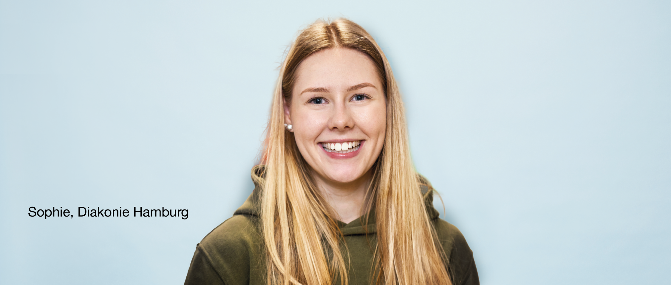 Person mit langen Haaren lächelt vor hellblauem Hintergrund. Text links: 'Sophie, Diakonie Hamburg'.